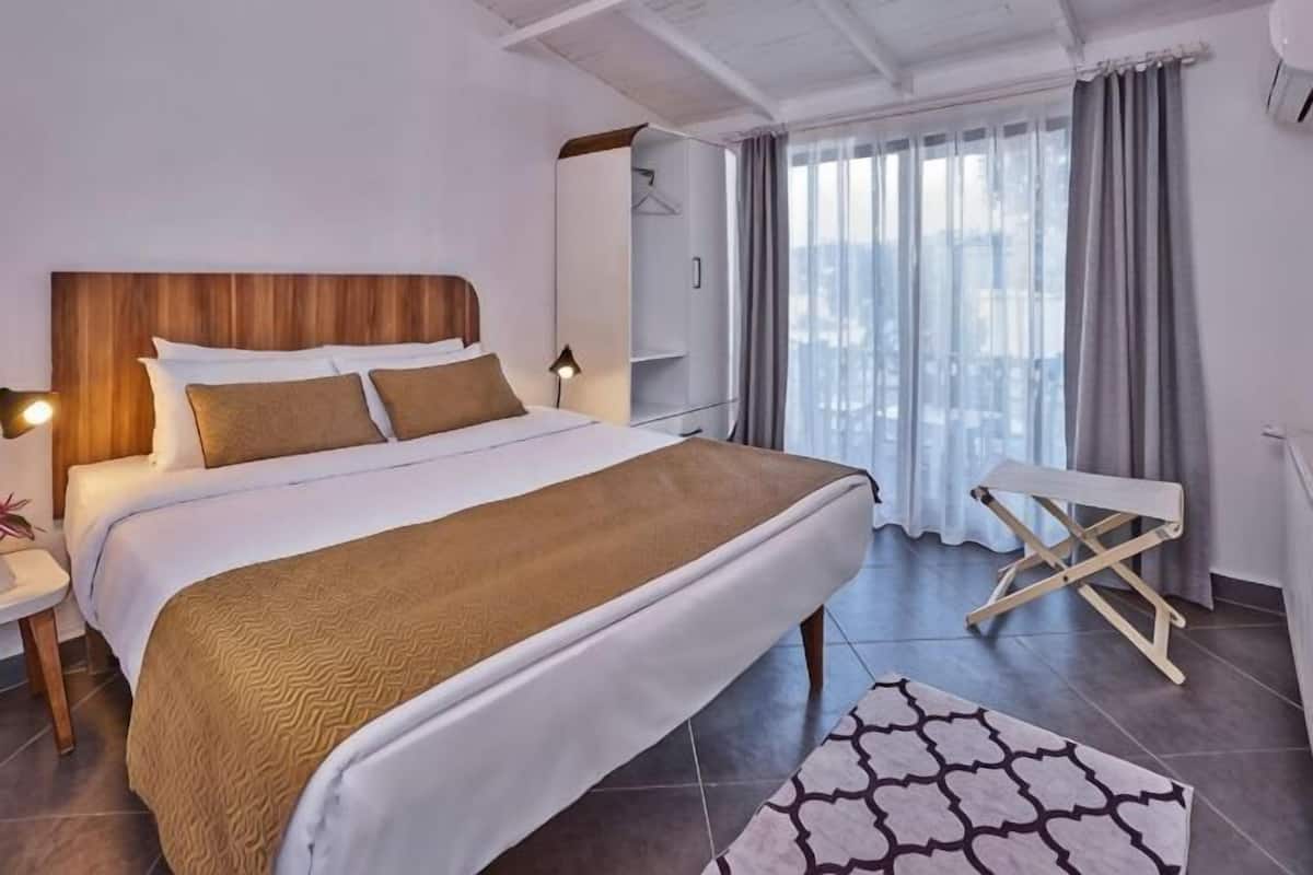 Une chambre d’hôtel avec un grand lit, des tables de chevet, un banc, une fenêtre avec des rideaux et une vue.