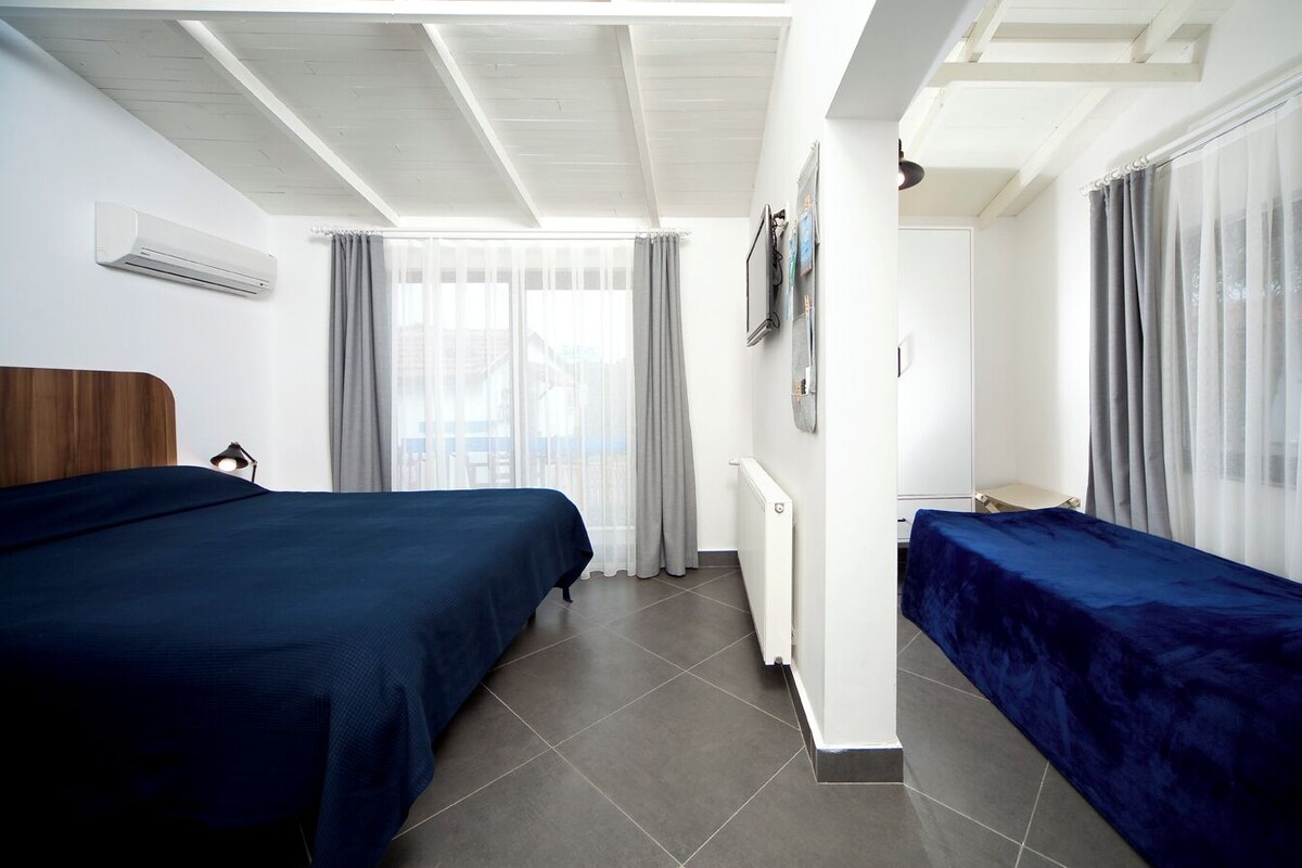 A hotel room with two beds, a ceiling fan, a radiator, and a window with curtains.