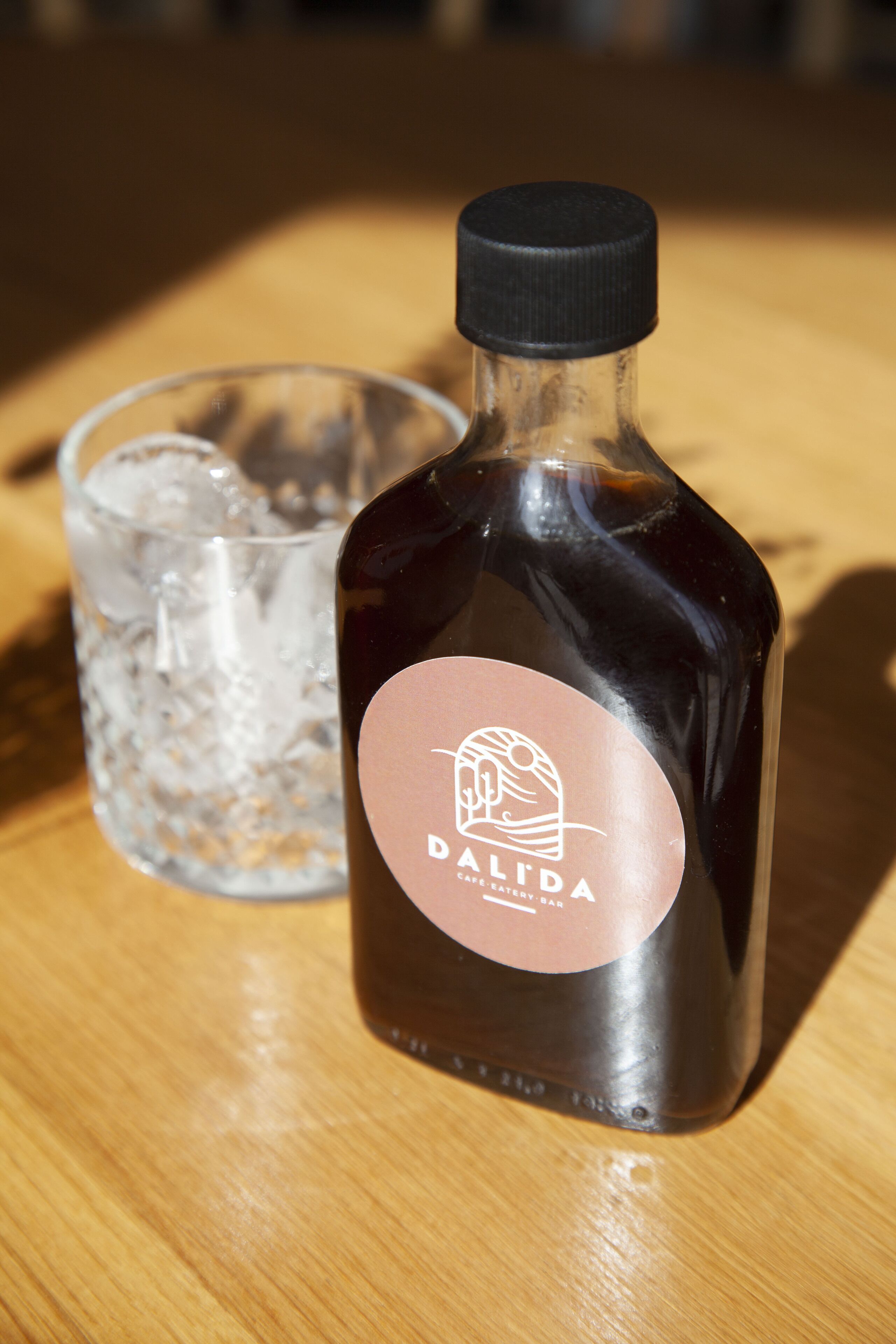 Une bouteille de vin Dalida et un verre d’eau glacée sur une table en bois.