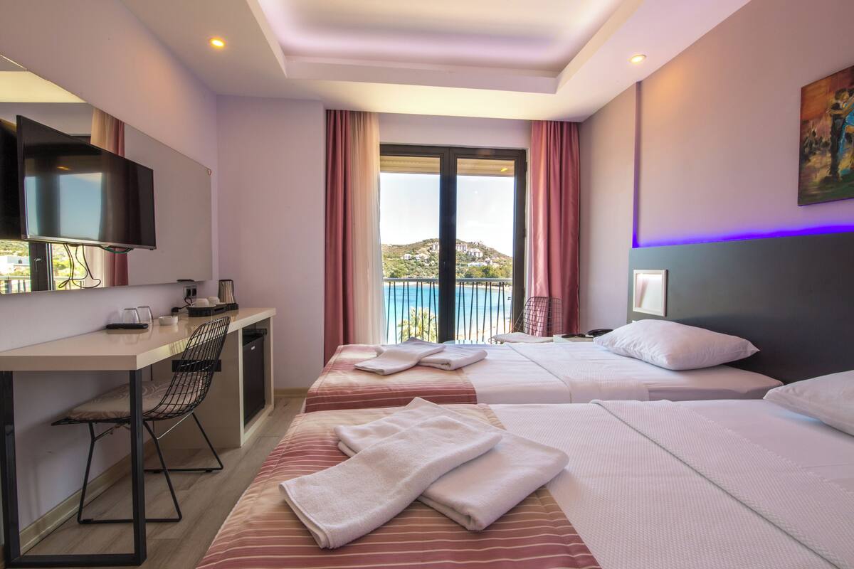 A hotel room with two beds, a desk, a chair, and a TV.