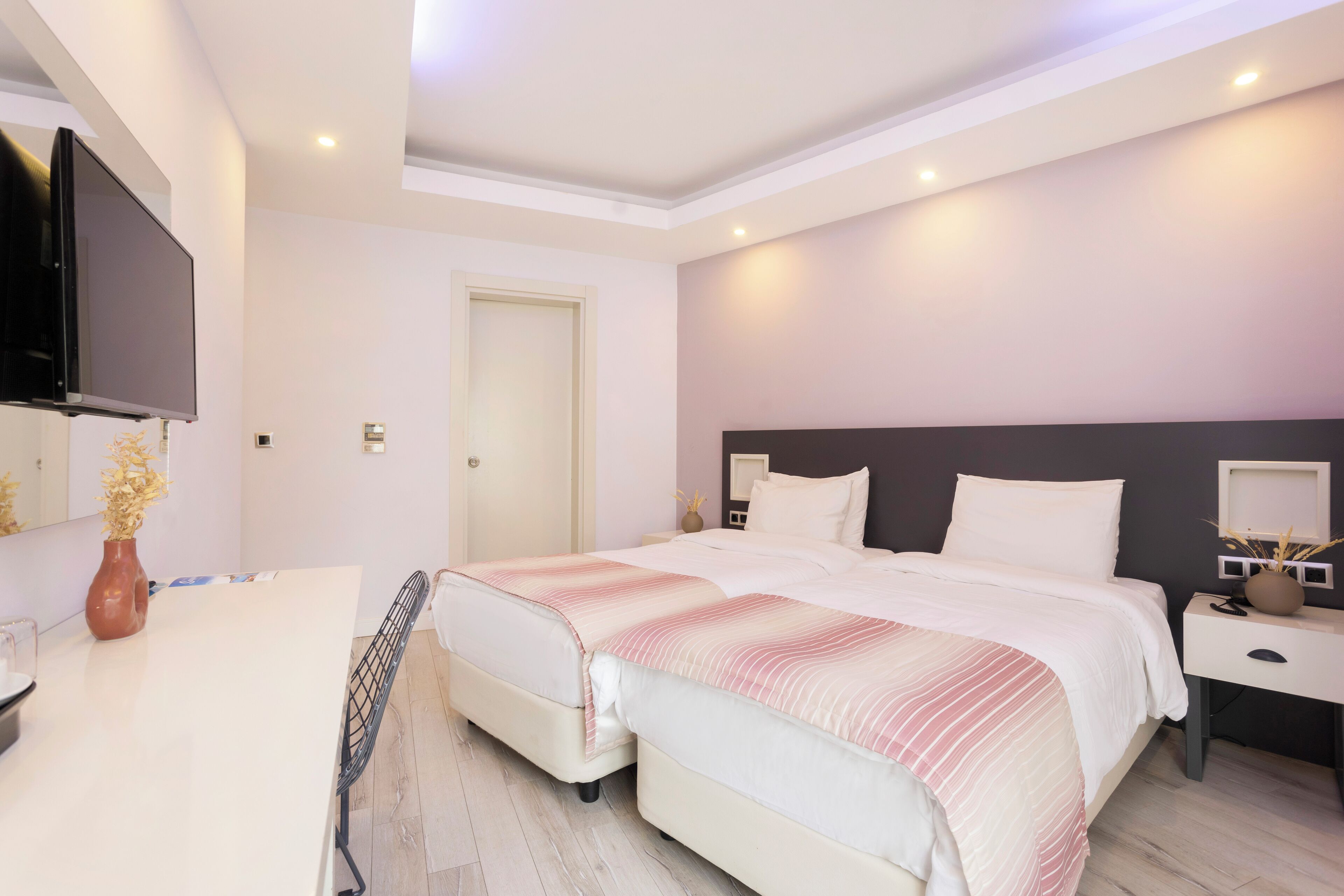 A modern bedroom with a large bed, bedside tables, a flat-screen TV, and a door.