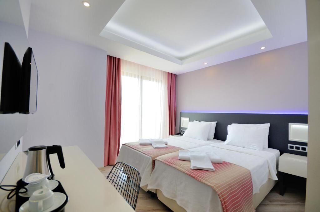 A hotel room with two beds, a desk with a coffee maker, a TV mounted on the wall, and a window with curtains.