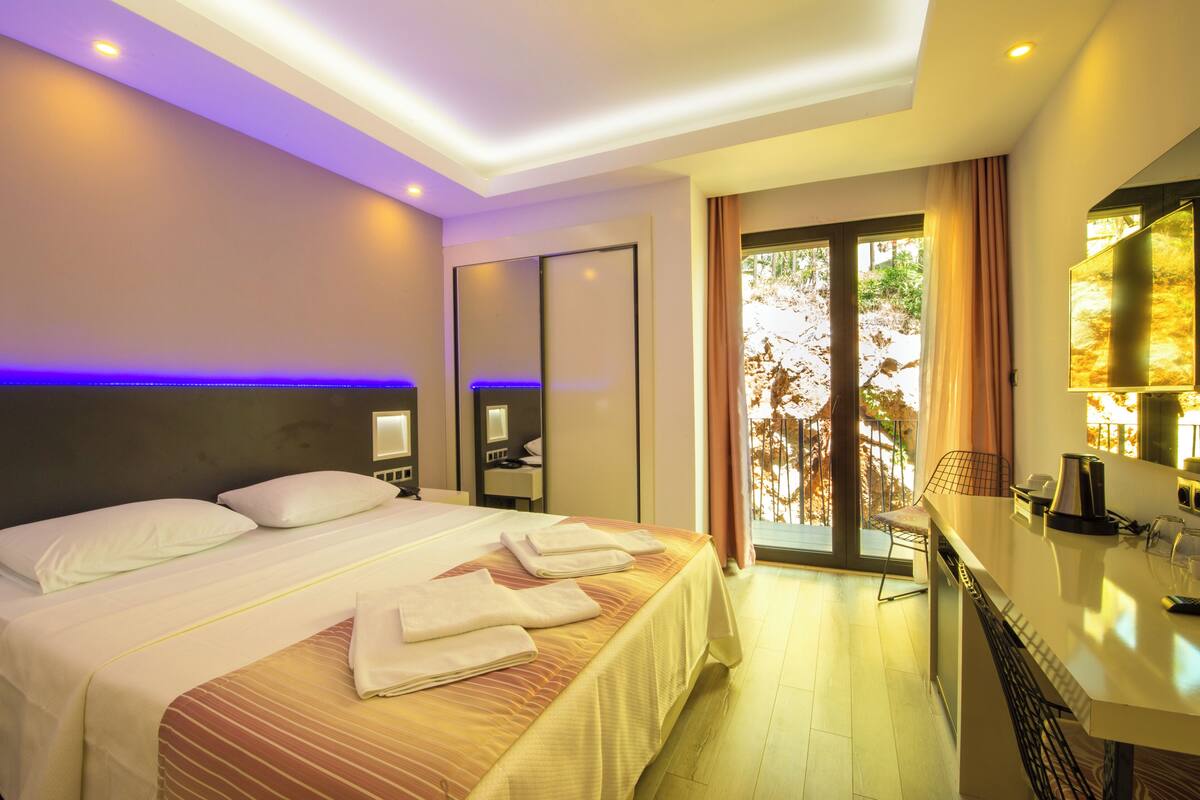 A hotel room with a bed, bedside tables, a desk, a chair, and a view of the outdoors.