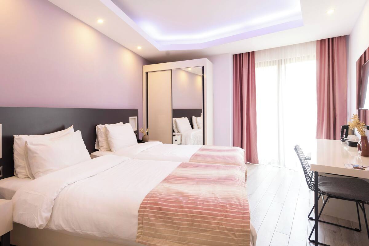 A hotel room with two beds, a desk, and a large mirror.