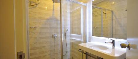 Un baño moderno con ducha de vidrio, lavamanos blanco y un espejo grande.