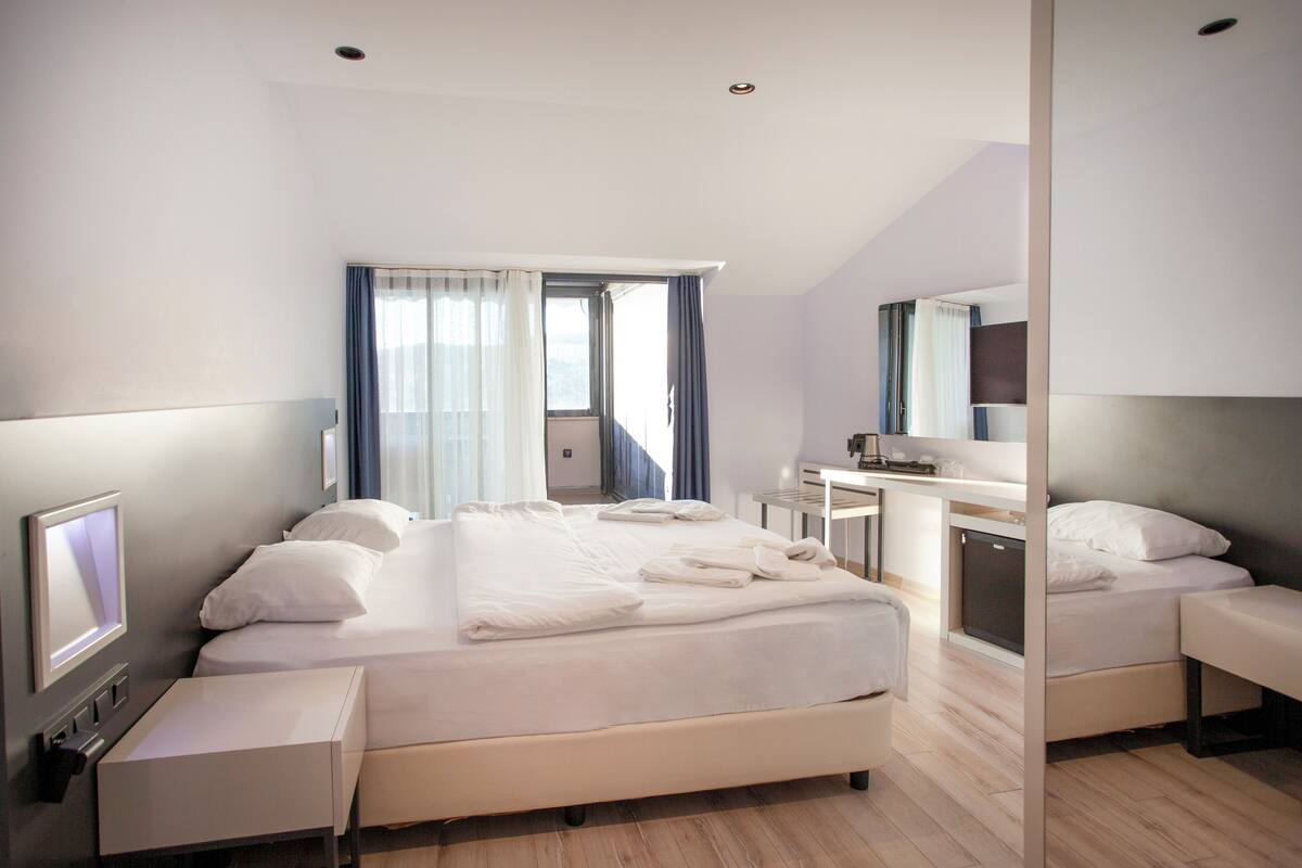 A modern hotel room with a large bed, a desk, and a mirror.