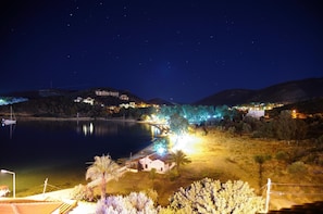 A nighttime view of a lakeside area with illuminated buildings, a dock with a boat, and a clear sky.