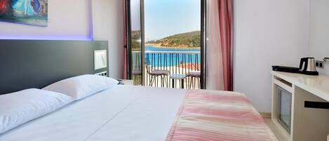 A hotel room with a bed, a painting, a balcony with a view, and a kitchenette.