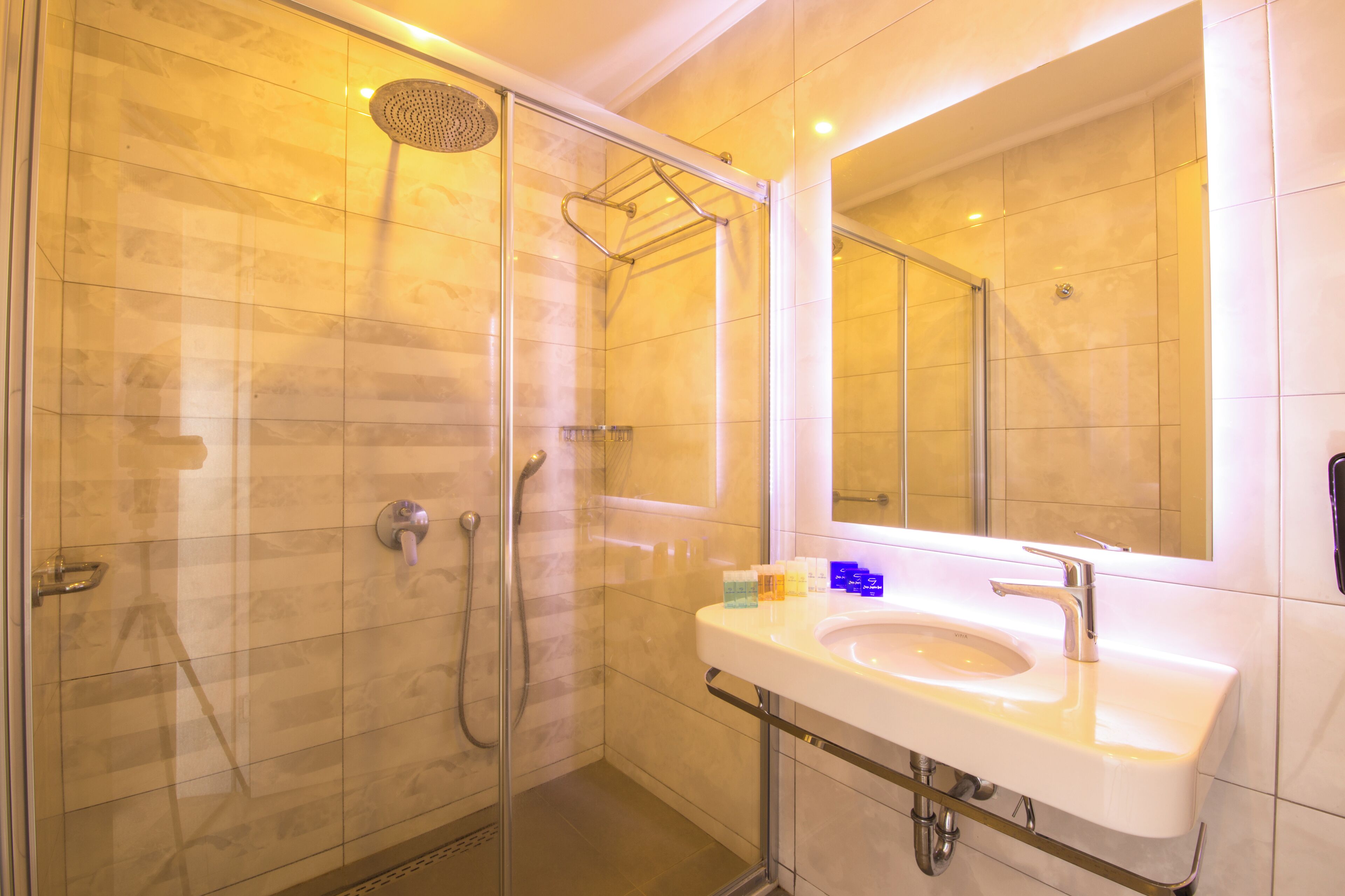 Un baño moderno con ducha de vidrio, un lavamanos blanco y un espejo grande.