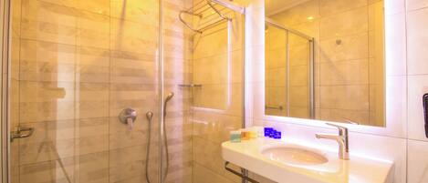 Un baño moderno con ducha de vidrio, un lavamanos blanco y un espejo grande.