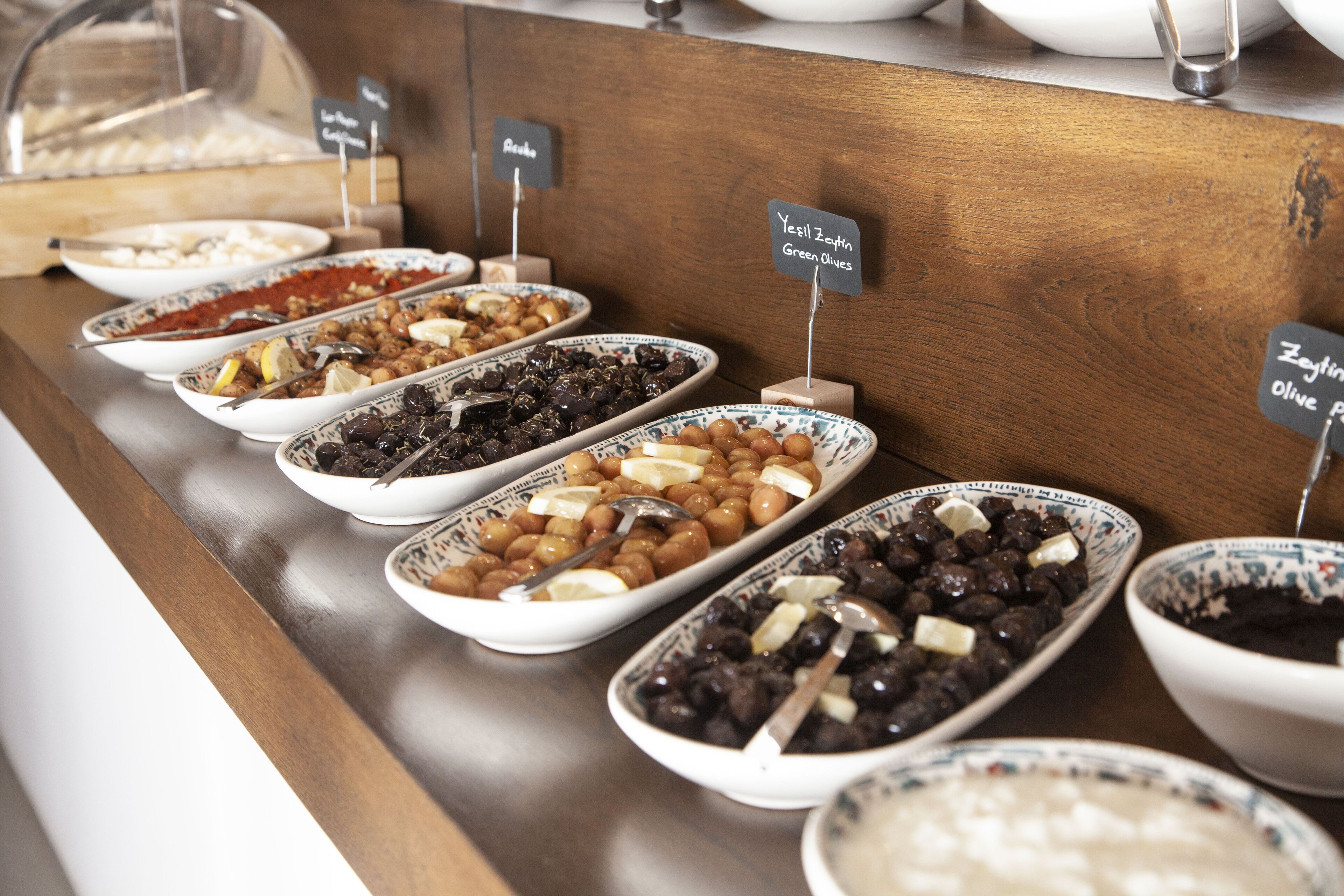 A buffet with various dishes labeled, including 'Yesil Zeytin Green Olives' and 'Zeytin Olive P'.