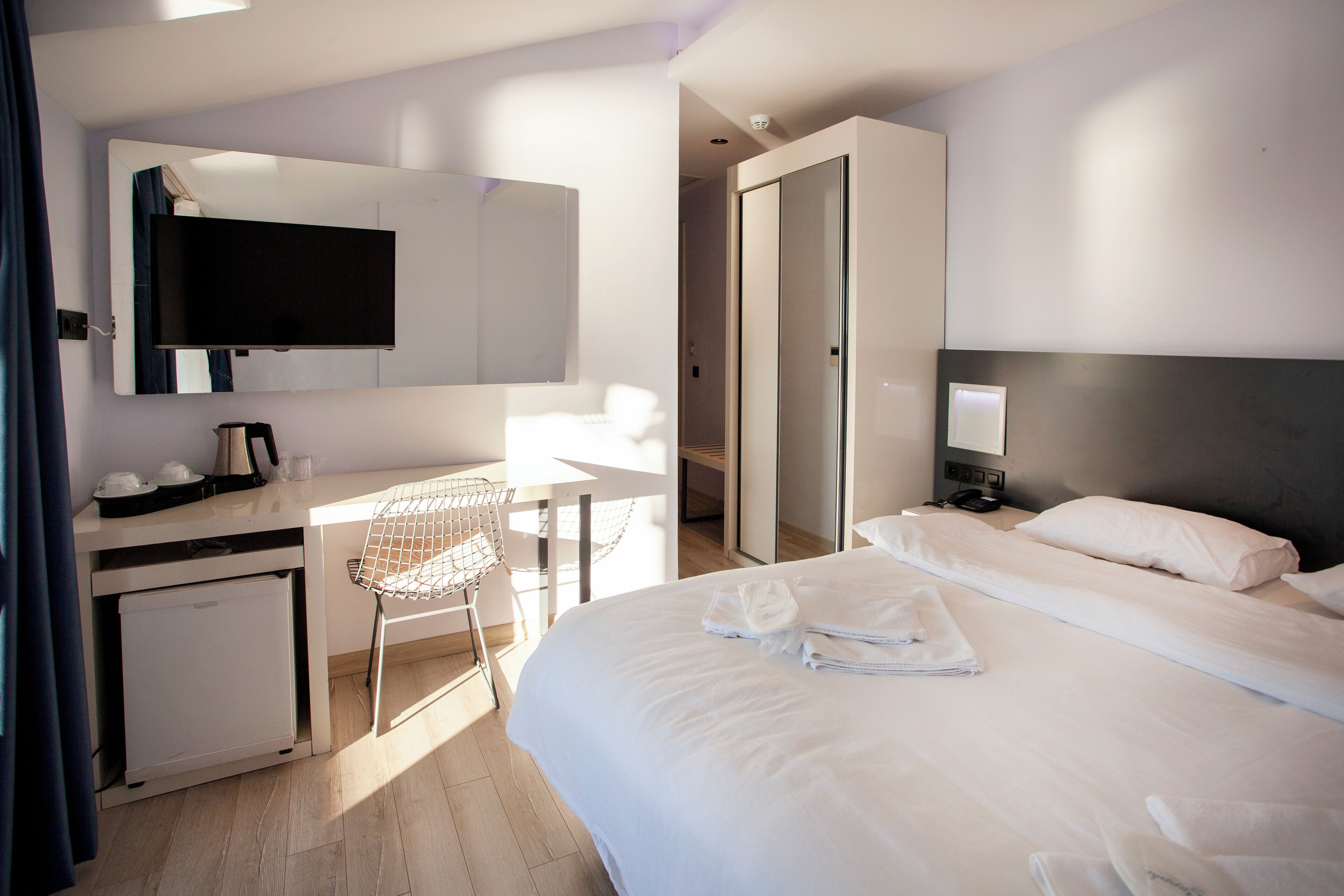 Ein Hotelzimmer mit Bett, Schreibtisch mit Stuhl, Fernseher und kleinem Kühlschrank.
