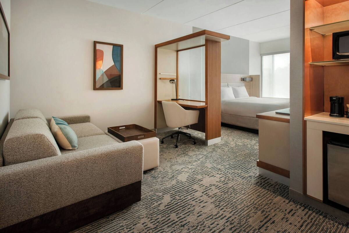 A hotel room with a bed, a desk, a chair, a sofa, a TV, and a coffee machine.