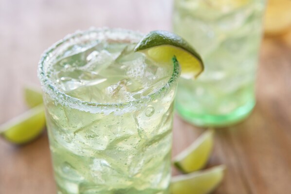 A glass of a clear, lime-flavored beverage with ice cubes and a lime slice garnish.