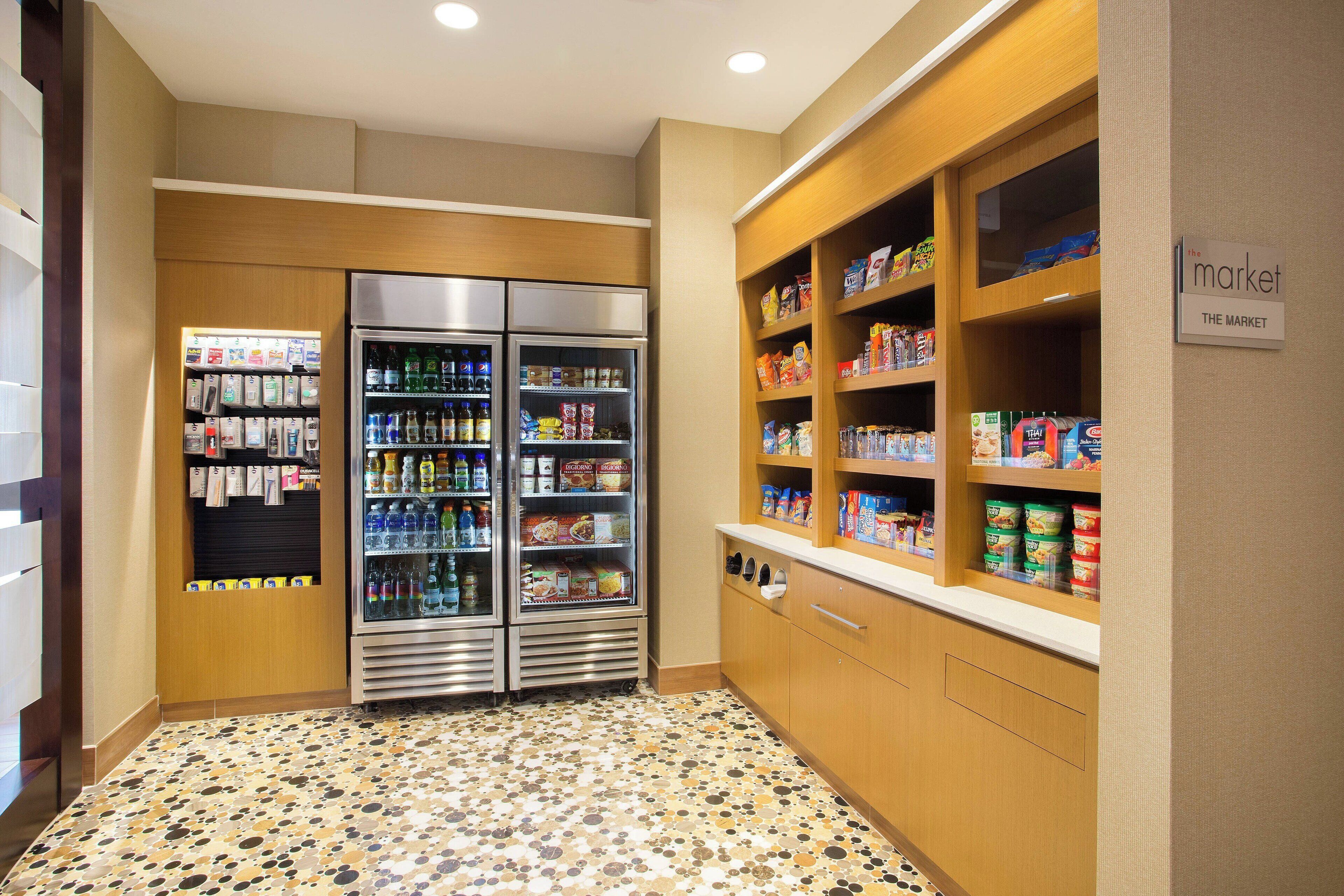 Una kitchenette equipada con refrigerador, microondas y cafetera. Se observan estantes con bocadillos y bebidas.