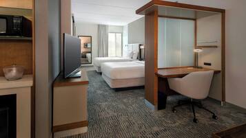 Habitación de hotel con televisor, dos camas, escritorio, silla, microondas y un espejo grande.
