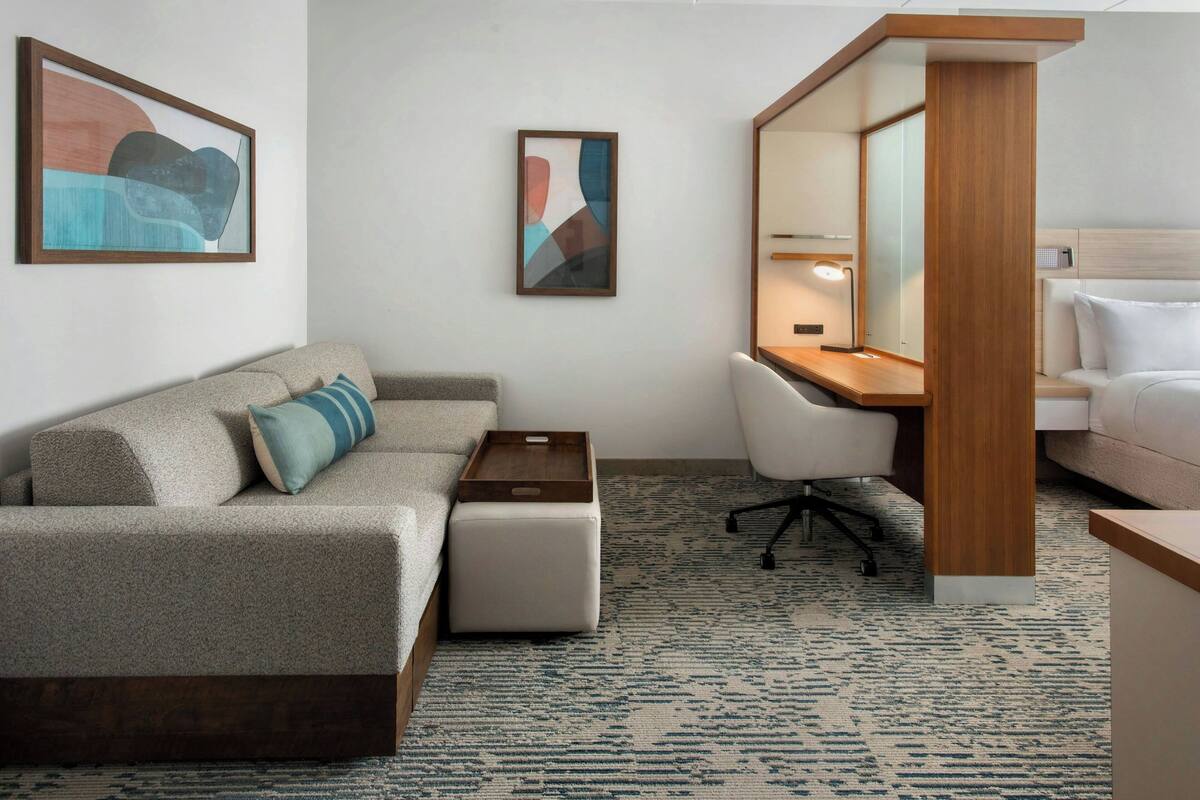 A hotel room with a sofa, a desk, a chair, a bedside table, and a bed.