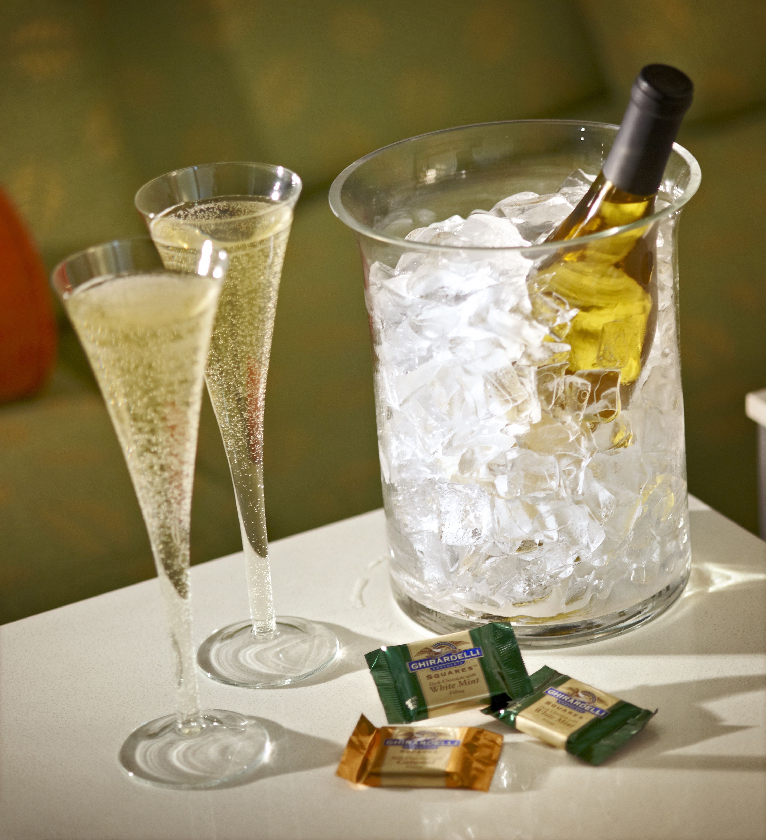 Two champagne flutes and a bottle of champagne in a glass container with ice cubes.
