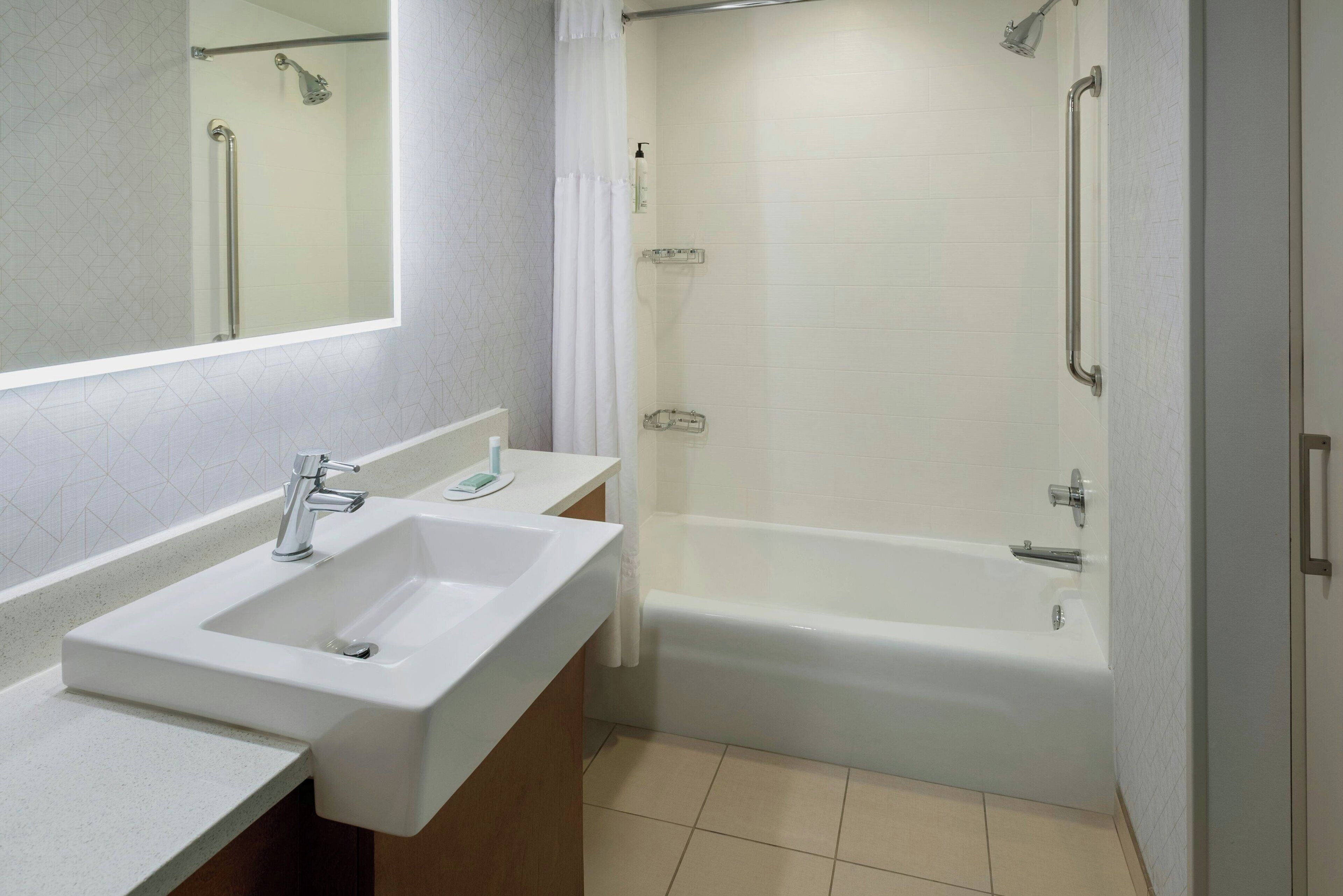 A modern bathroom with a white sink, vanity, and bathtub.