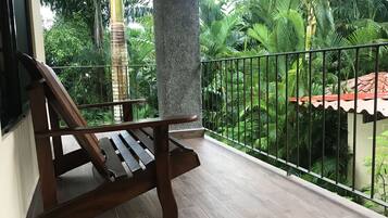A wooden bench on a balcony with a view of lush greenery and a tiled floor.