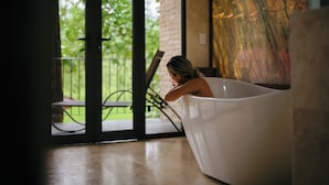 Une personne se détend dans une baignoire, avec vue sur un patio et la verdure environnante.