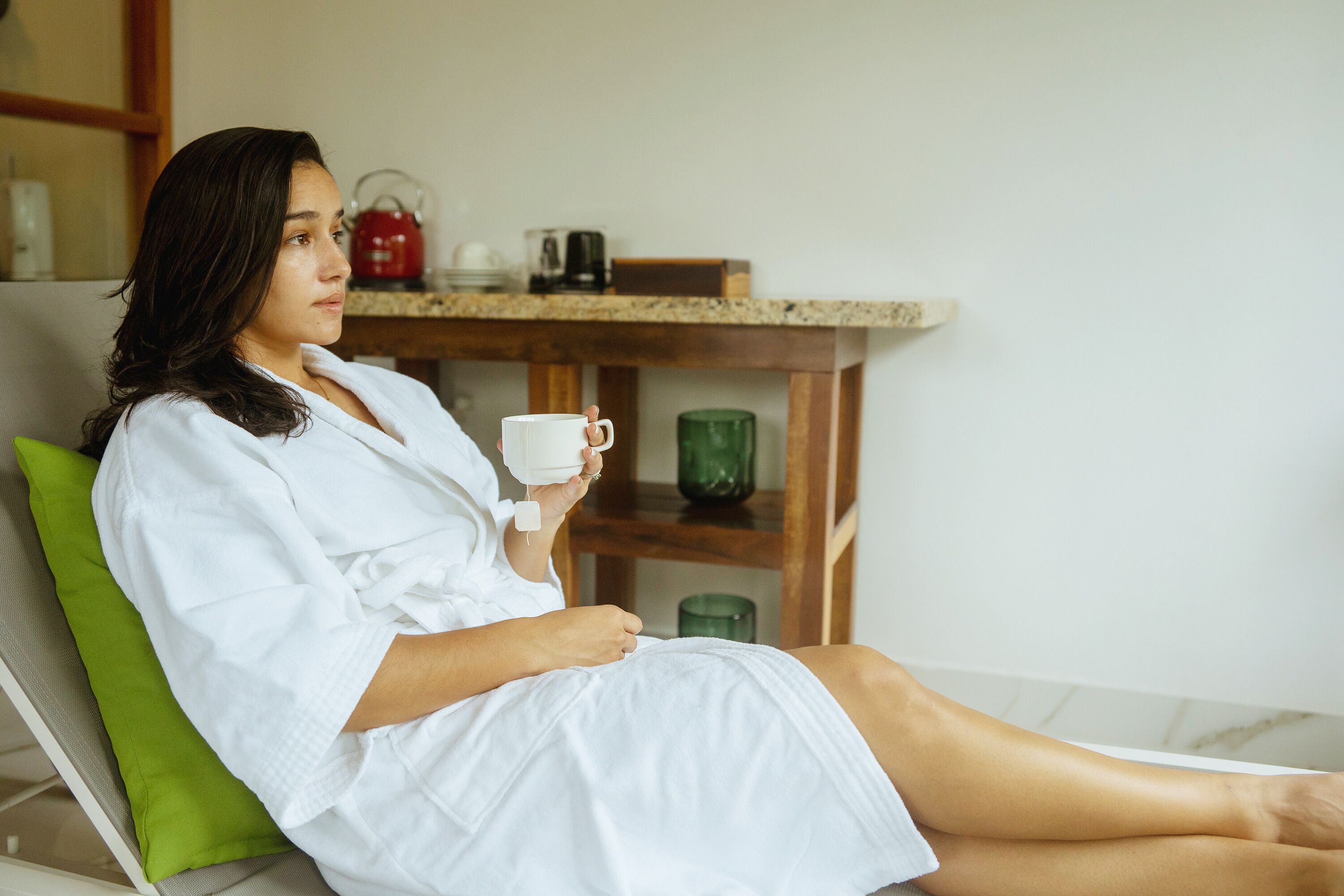 A person sitting on a green chair in a room with a wooden table and a white wall.