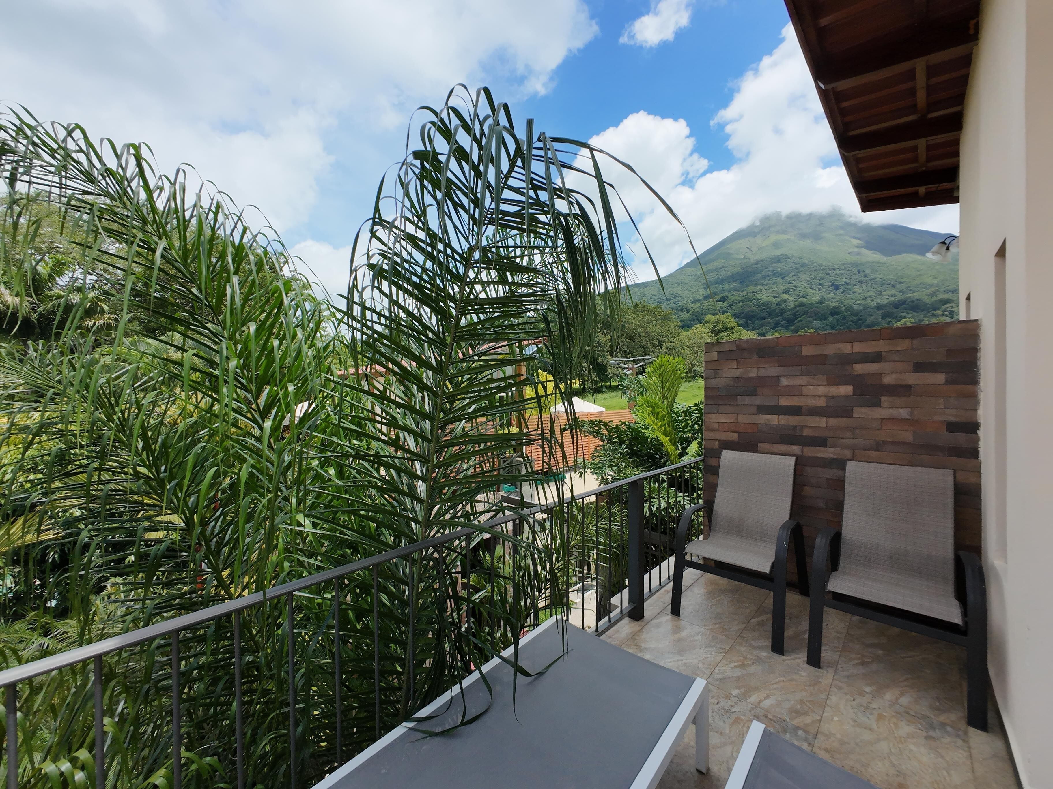Un balcón con vistas a un jardín exuberante y montañas a lo lejos.