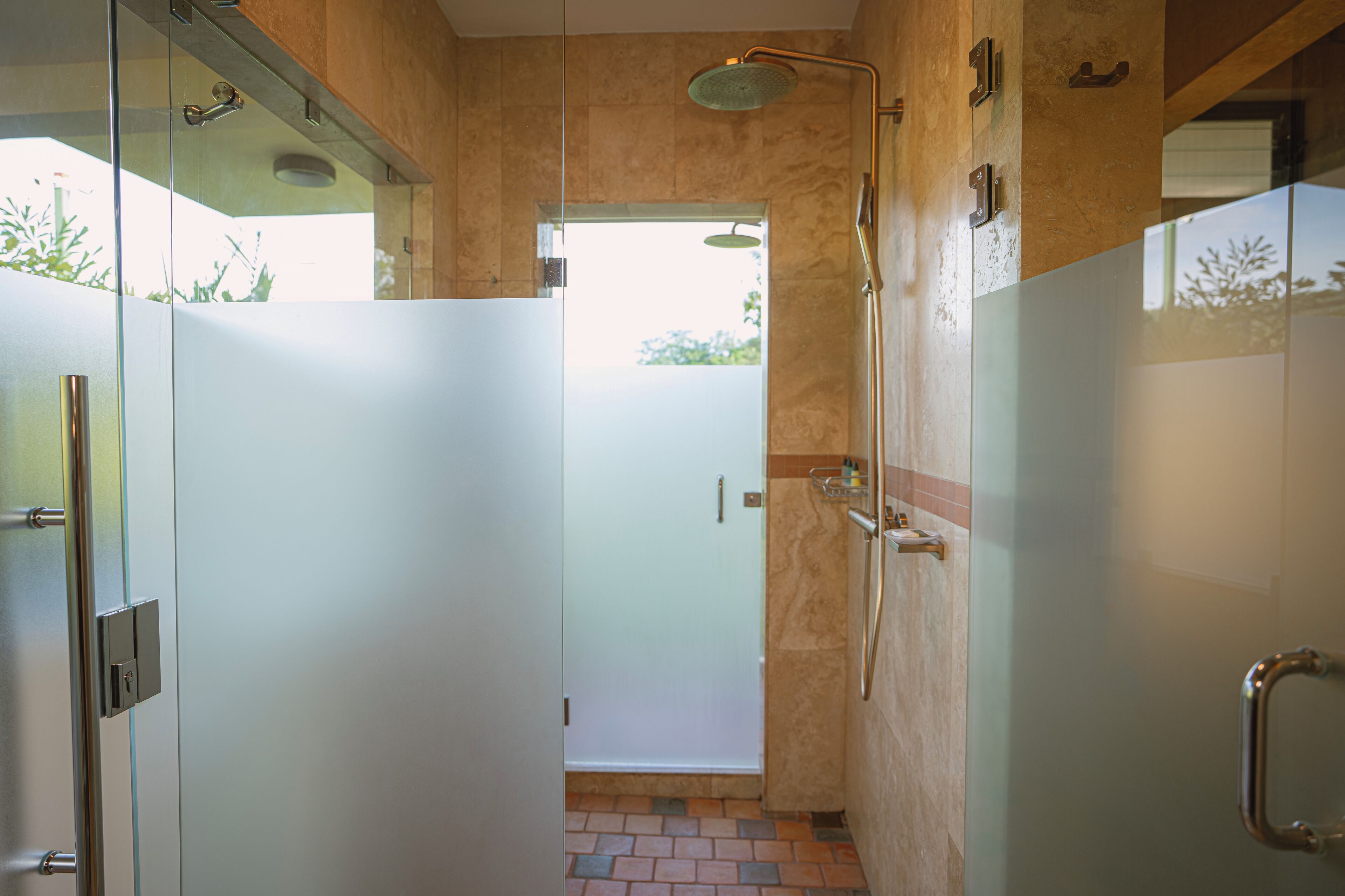 A modern bathroom with a glass shower enclosure, a walk-in shower, and a glass door leading to a tiled area.