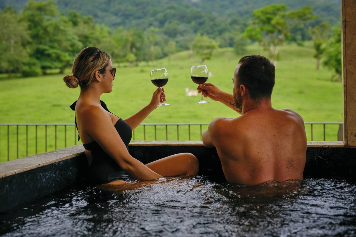 Deux personnes dans un jacuzzi, avec vue sur un paysage verdoyant.