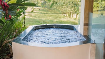 A hot tub with a view of a lush garden and a grassy field.