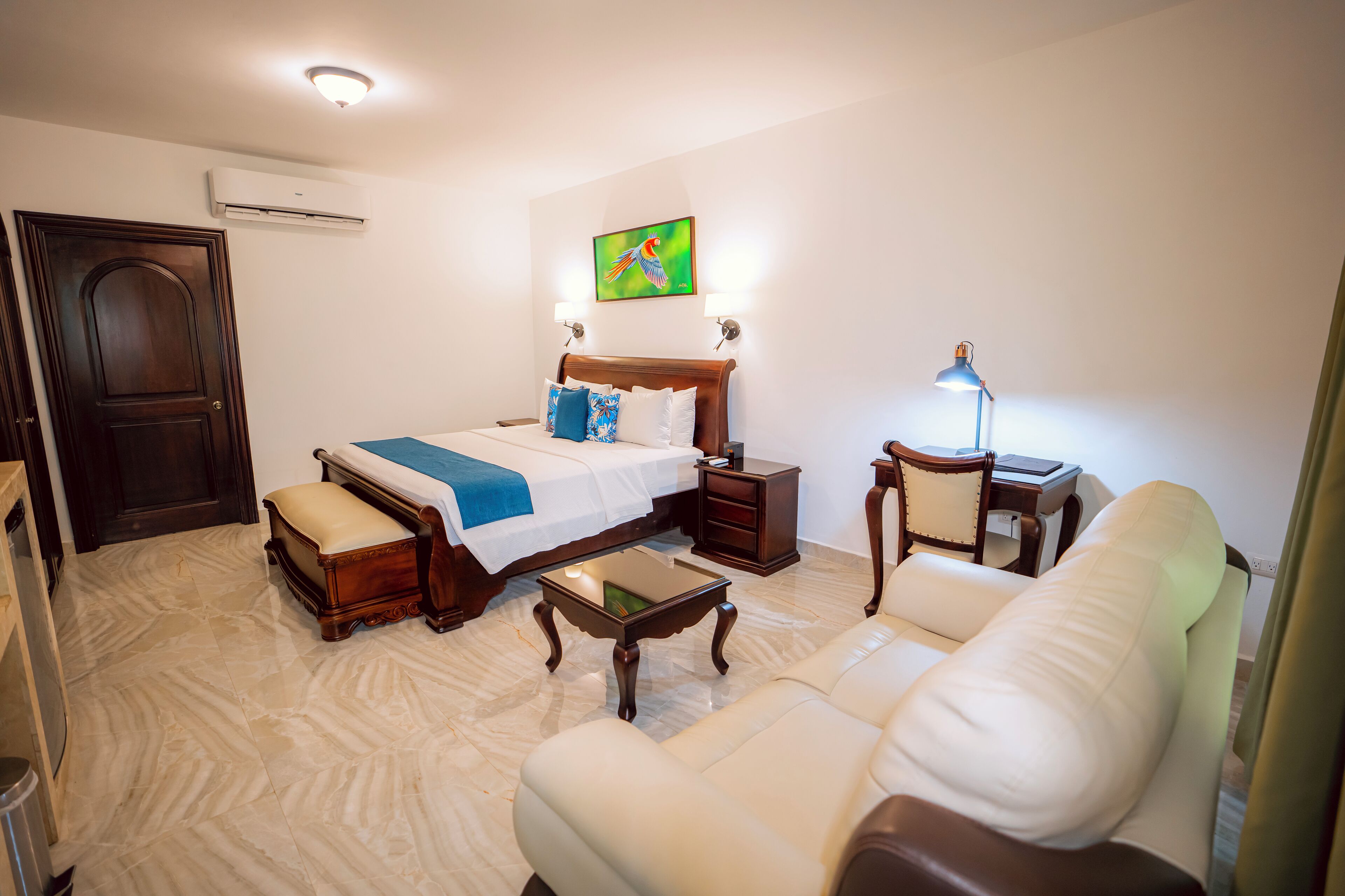A hotel room with a bed, a sofa, a nightstand, a lamp, and a painting on the wall.