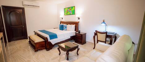 A hotel room with a bed, a sofa, a nightstand, a lamp, and a painting on the wall.