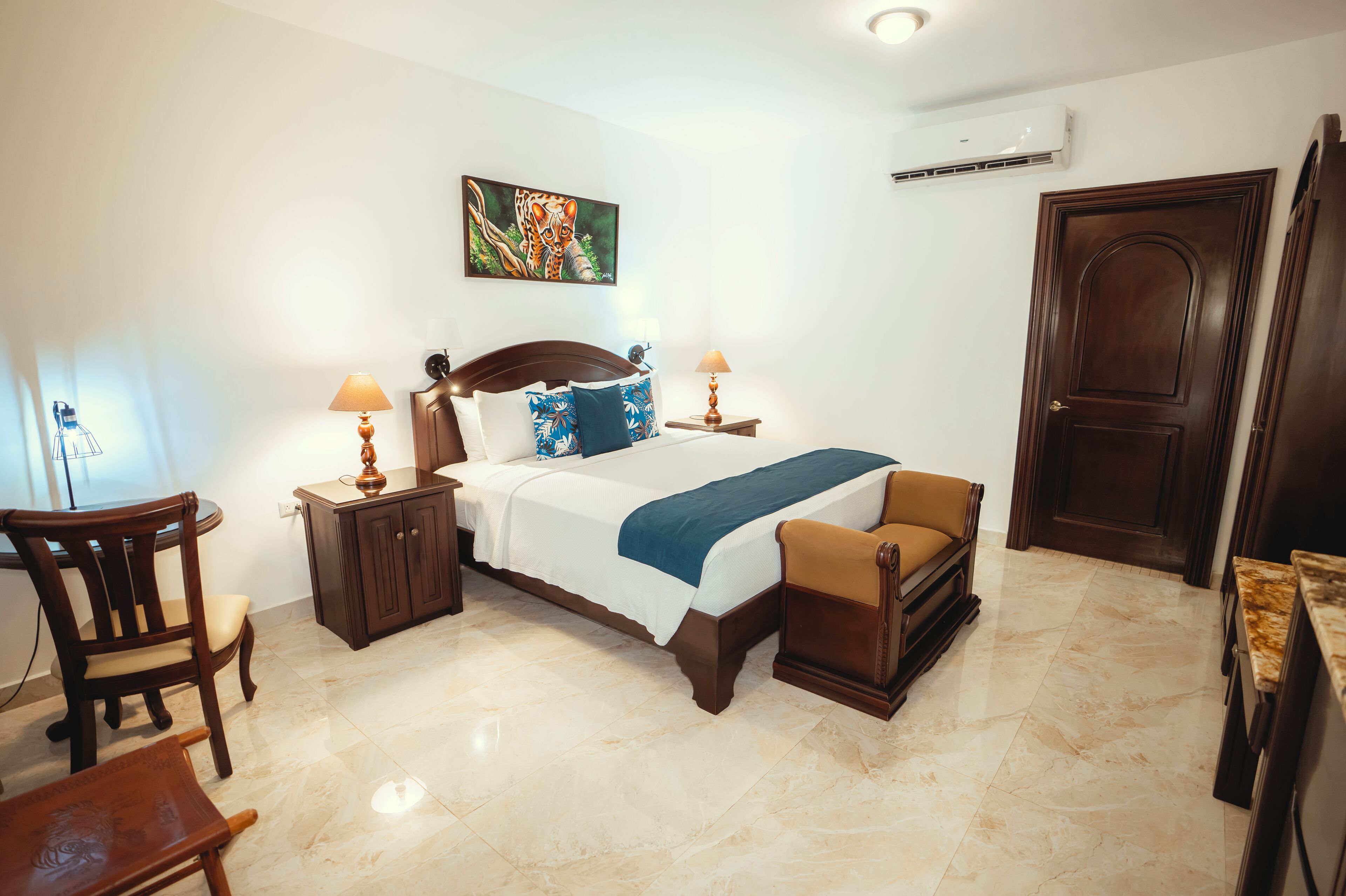 A hotel room with a bed, a desk, a chair, a cabinet, and a door.