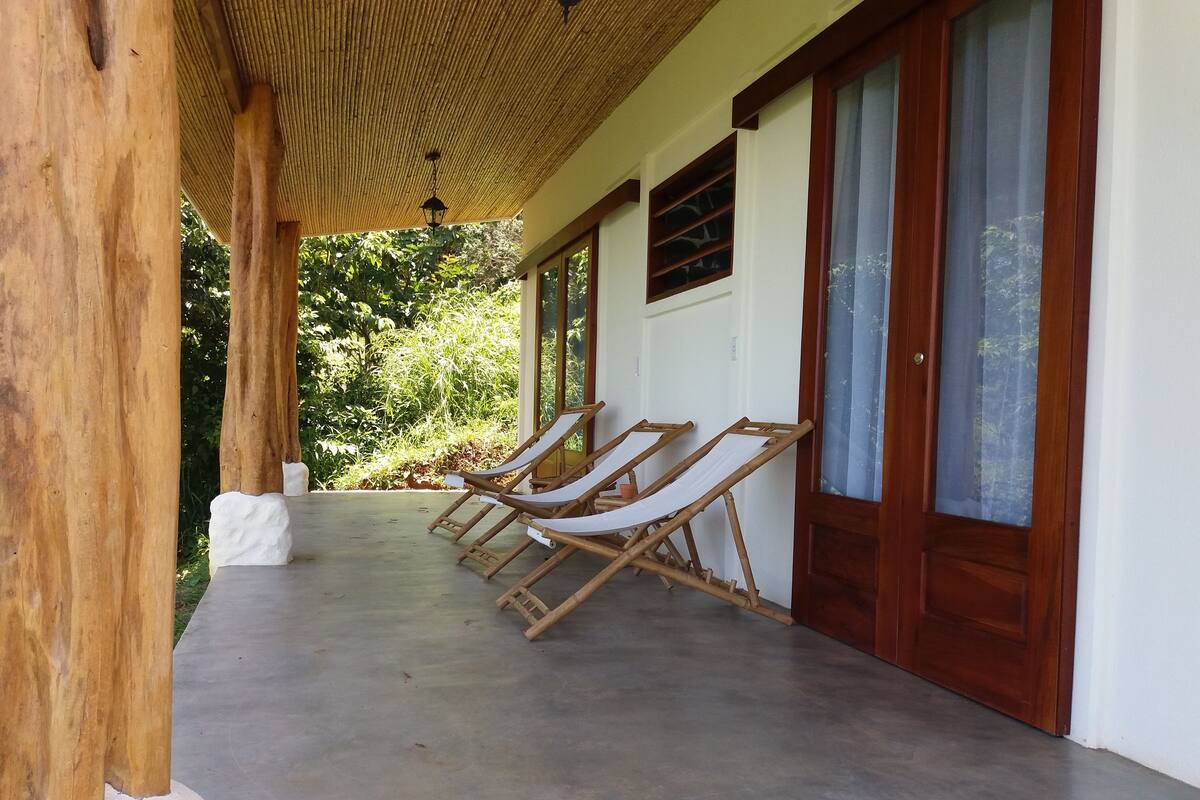 Eine überdachte Veranda mit drei Holzliegen und einem Betonboden.