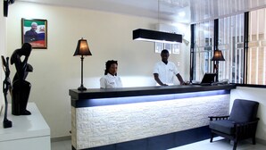Un comptoir d’accueil au design moderne, une grande fenêtre avec des stores et une sculpture sur le côté gauche.