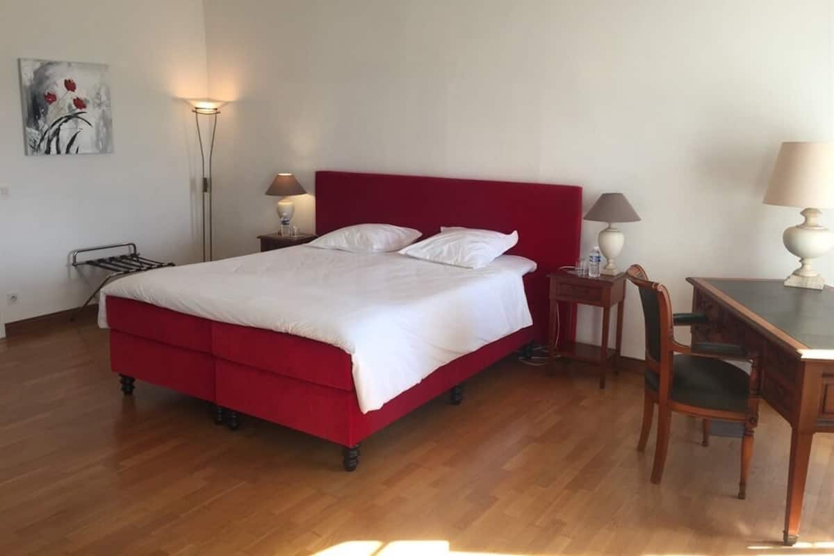 Een kamer met een rode bed, twee nachtkastjes met lampen, een houten bureau en een stoel.