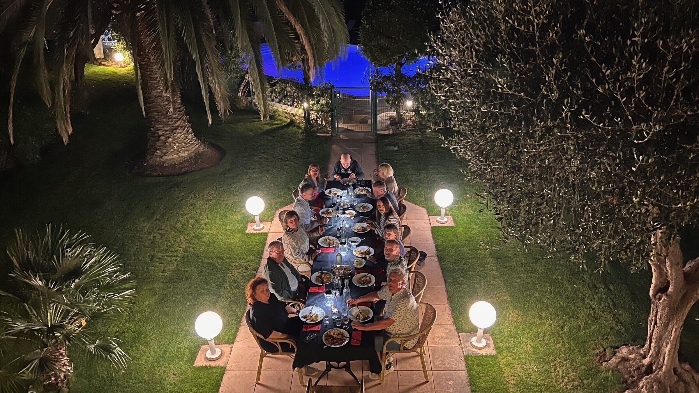 An outdoor dining area with a long table, chairs, and illuminated light fixtures.