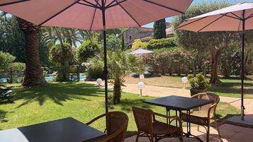 An outdoor patio with tables and chairs, surrounded by greenery and a pool.