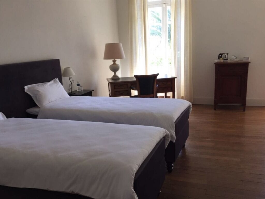 A hotel room with two beds, a desk with a lamp, a chair, and a small cabinet.