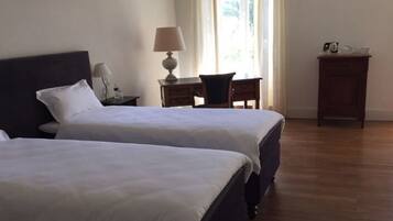 Ein Hotelzimmer mit zwei Betten, einem Schreibtisch mit Lampe, einem Sessel und einem kleinen Schrank.