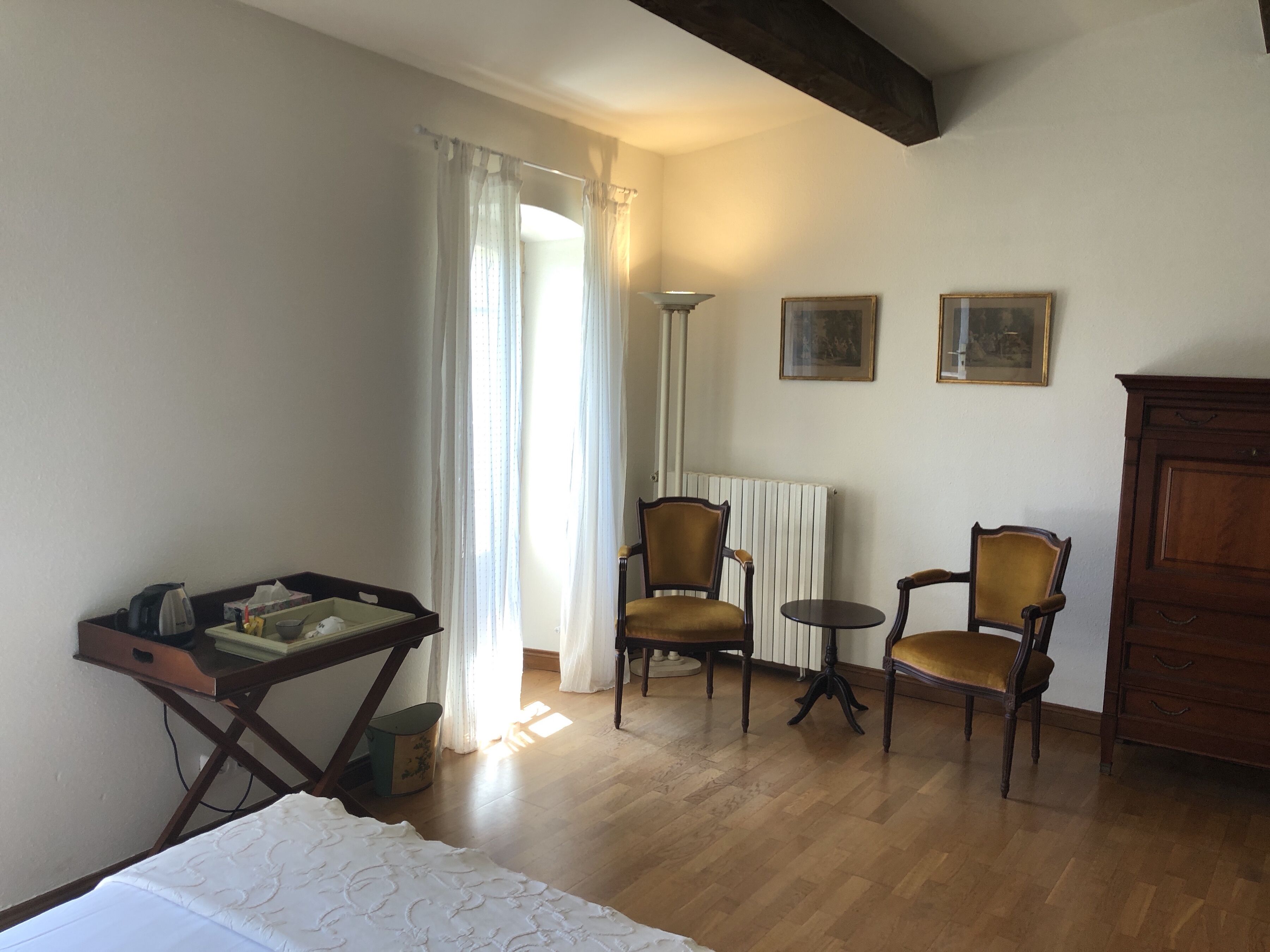 A room with a bed, two chairs, a table, a radiator, and a cabinet.