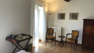 A room with a bed, two chairs, a table, a radiator, and a cabinet.