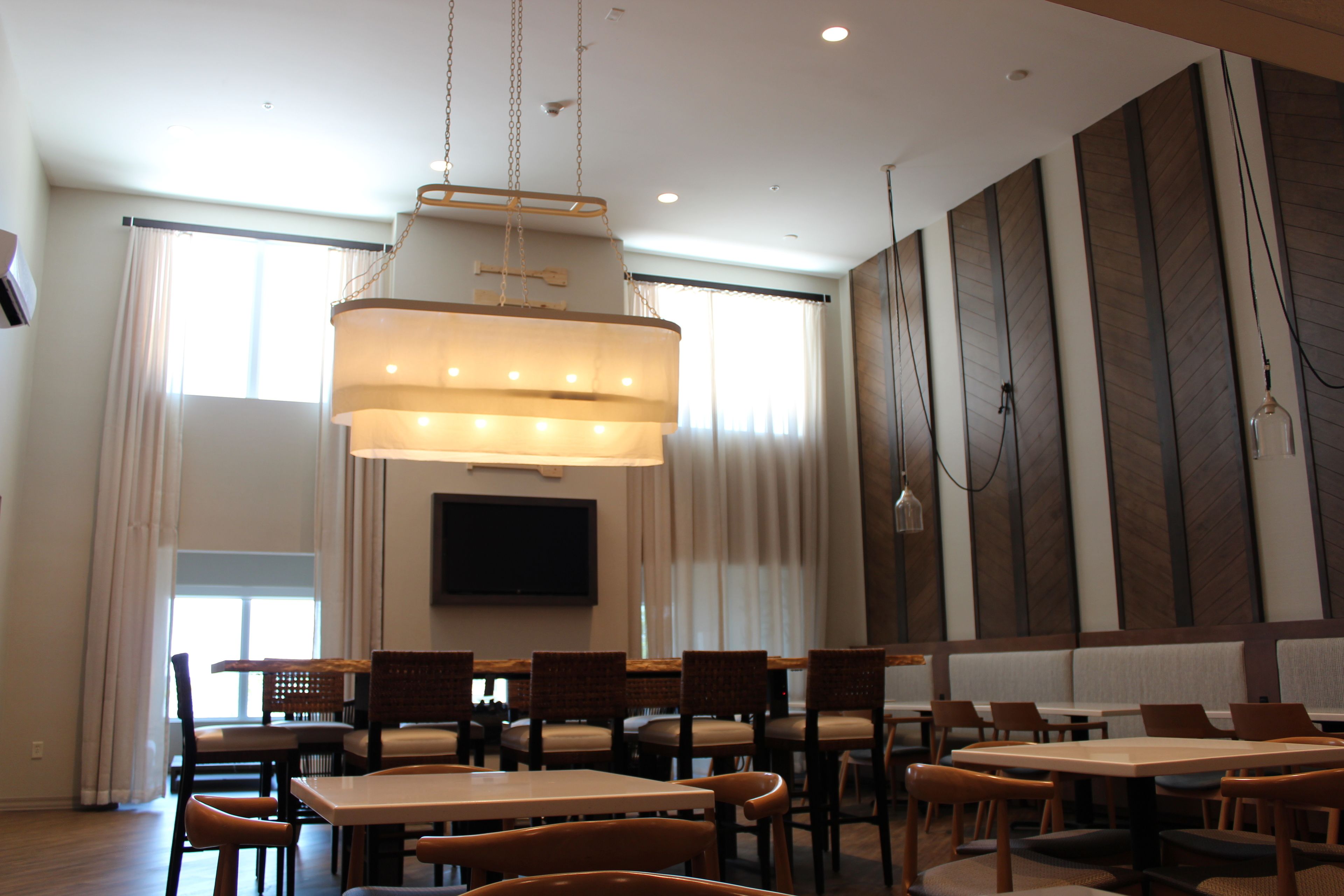 A dining area with multiple tables and chairs, a large chandelier, and a flat-screen TV mounted on the wall.