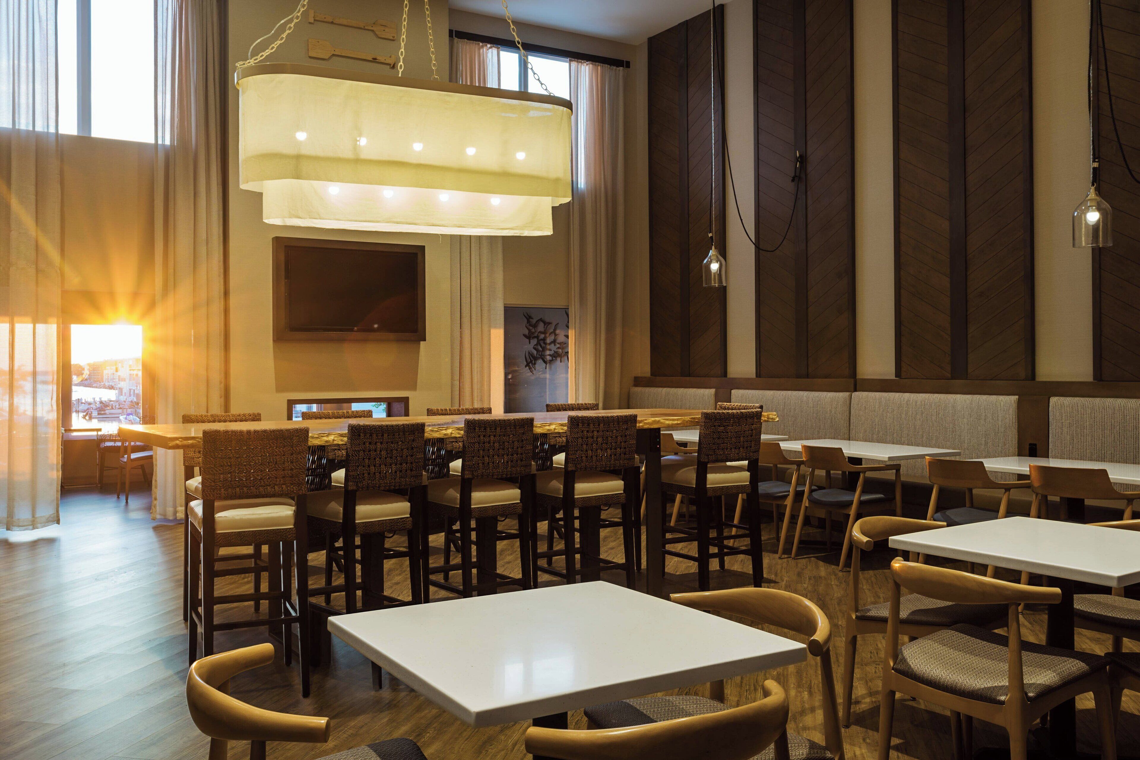 A restaurant with multiple tables and chairs, a large chandelier, and a television screen on the wall.