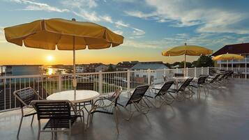Une terrasse avec des places assises extérieures, des parasols et une vue sur le coucher de soleil au-dessus d’un quartier résidentiel.
