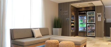 Eine moderne Hotelhalle mit einer Couch, Hocker und einem Kiosk mit gekühlten Getränken.