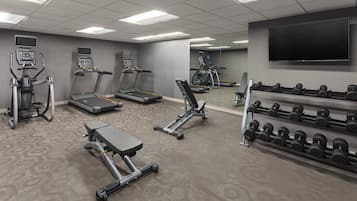 A gym with treadmills, elliptical machines, a bench press, and a rack of dumbbells.