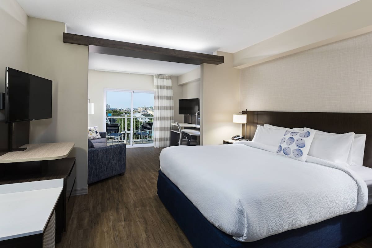 Una habitación de hotel con una cama grande, un escritorio, un televisor y un balcón con vistas a la ciudad.