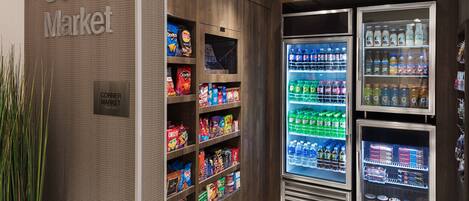 Uma mercearia de esquina com prateleiras repletas de lanches e bebidas, e uma seção refrigerada com bebidas e laticínios.