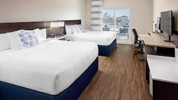 A hotel room with two beds, a desk, a chair, a TV, and a balcony with a city view.